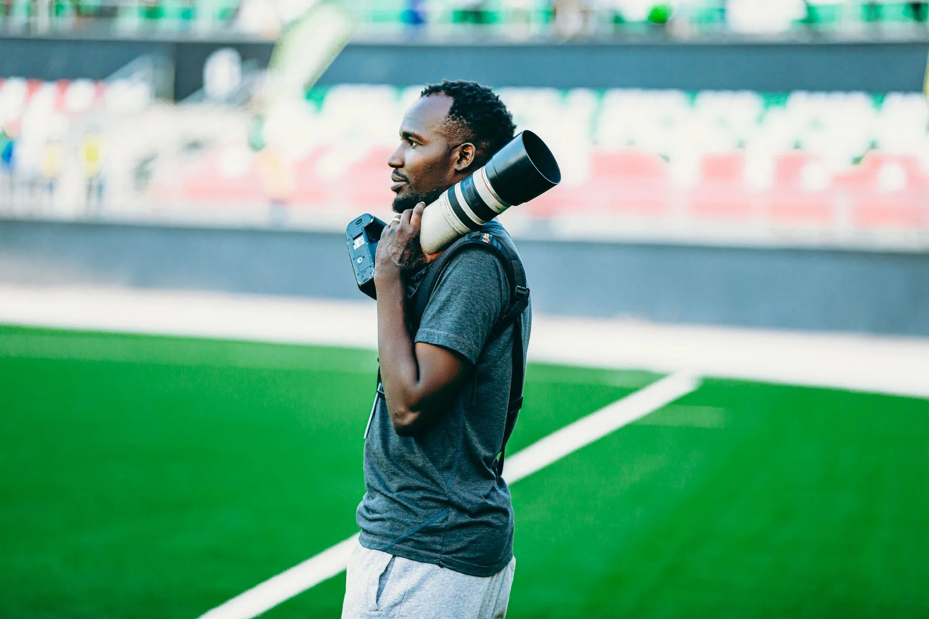 Photographe sportif portant un téléobjectif sur l'épaule au bord d'un terrain de football